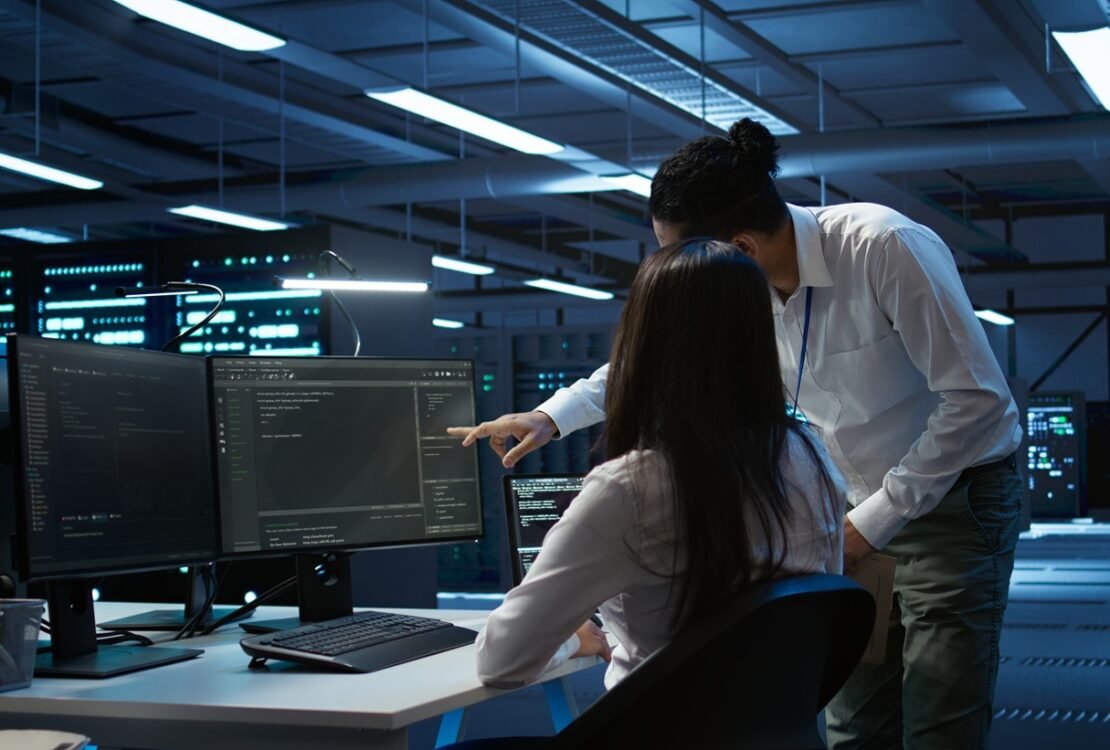 Dua teknisi IT sedang memantau sistem jaringan dan keamanan server infrastruktur IT bisnis di ruang data center